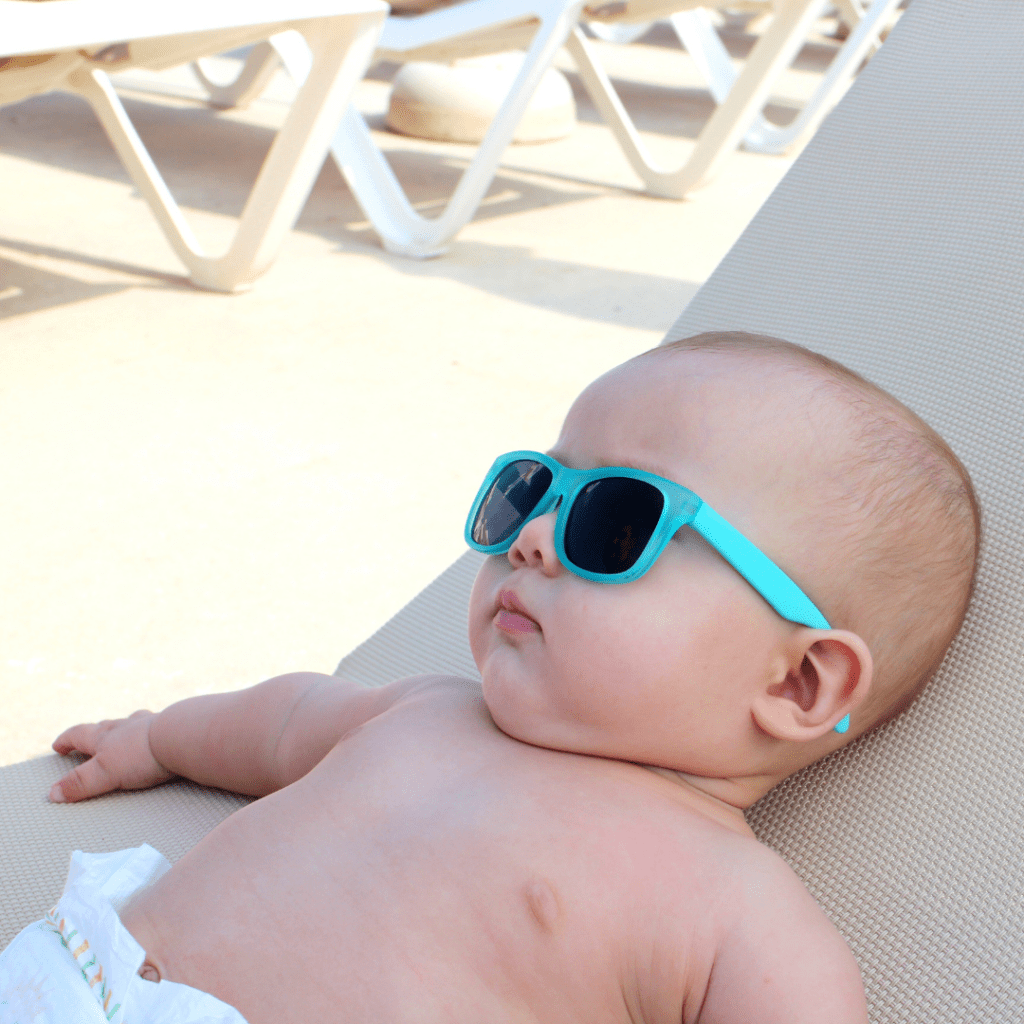Baby in a diaper laying on a beach chair with blue sunglasses.