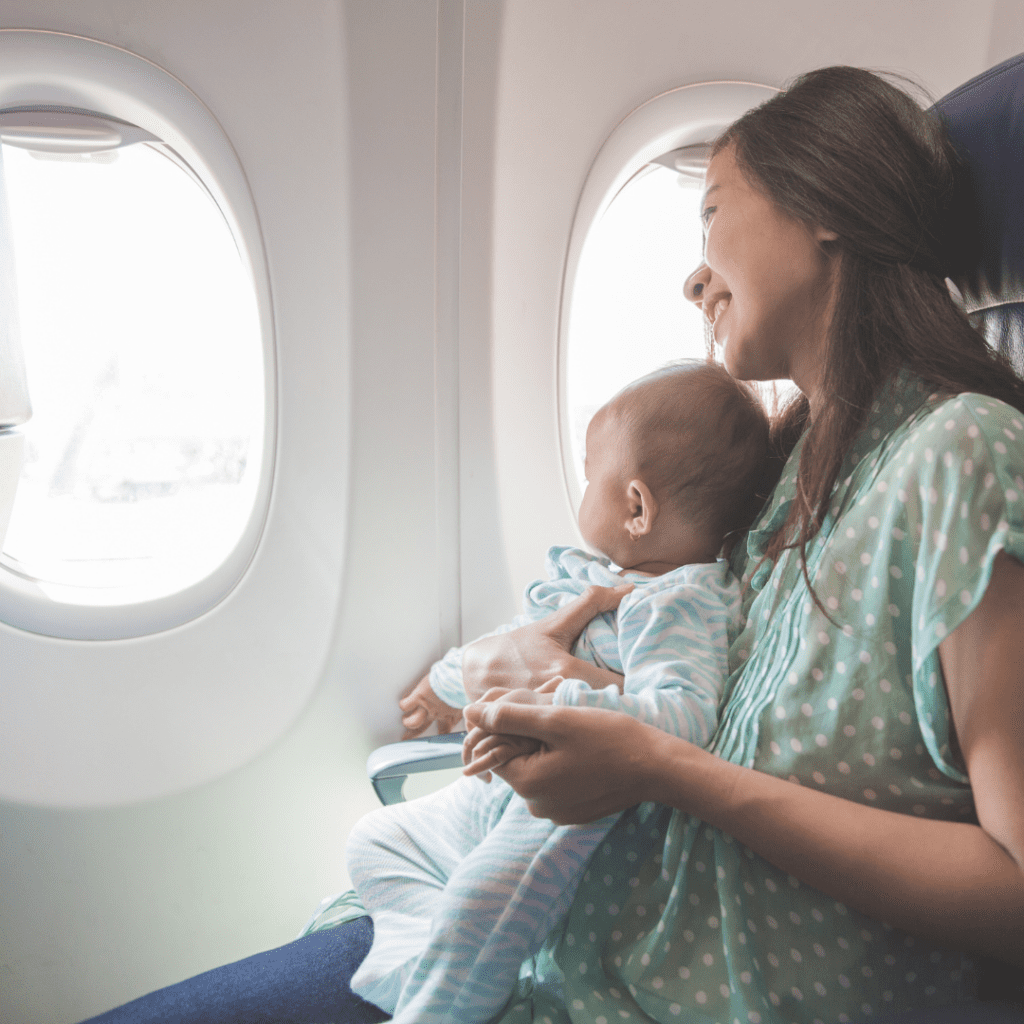 Baby sitting on mother looking at the window of an airplane.