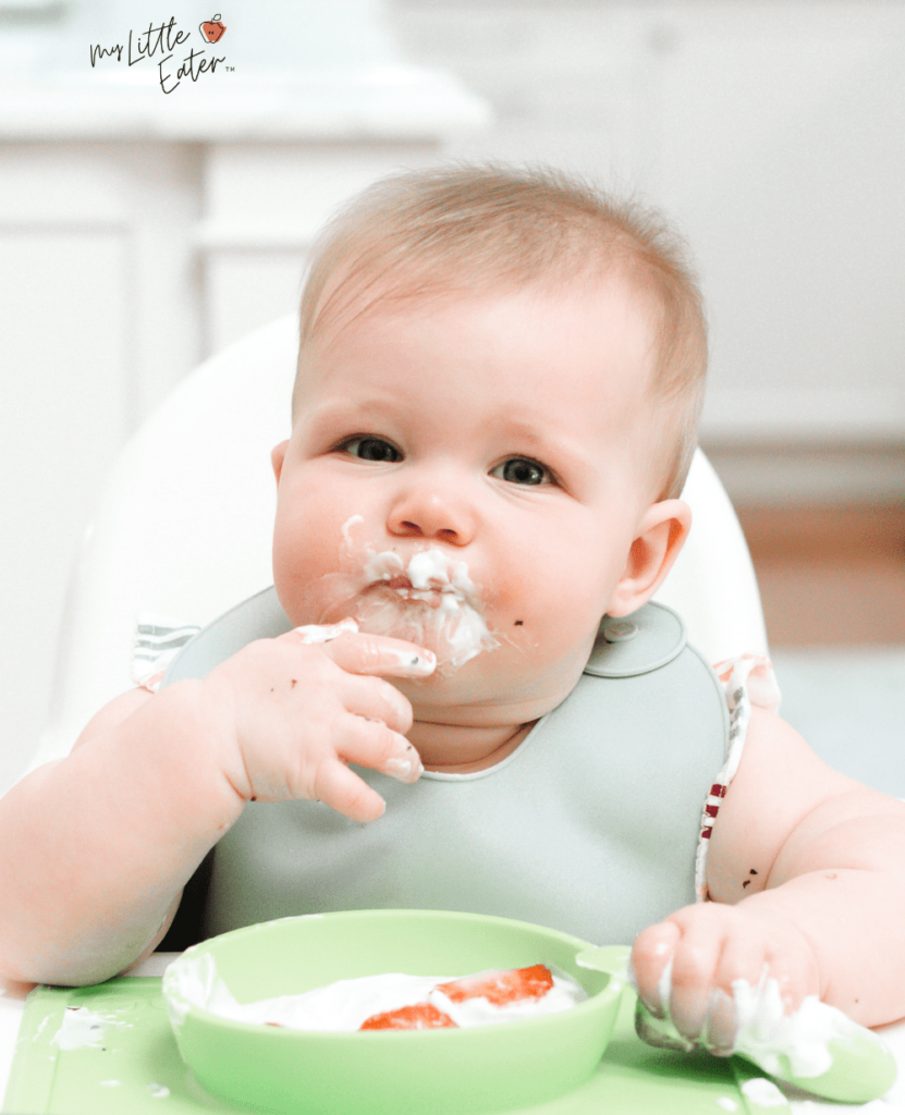 Baby eating yogurt and strawberries in their high chair.