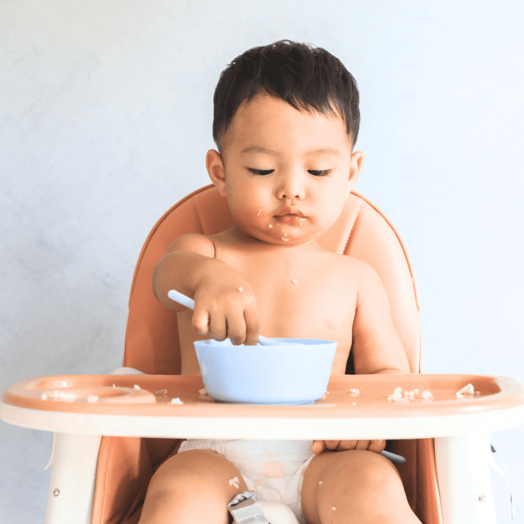A baby eating from a bowl while sitting in their high chair.
