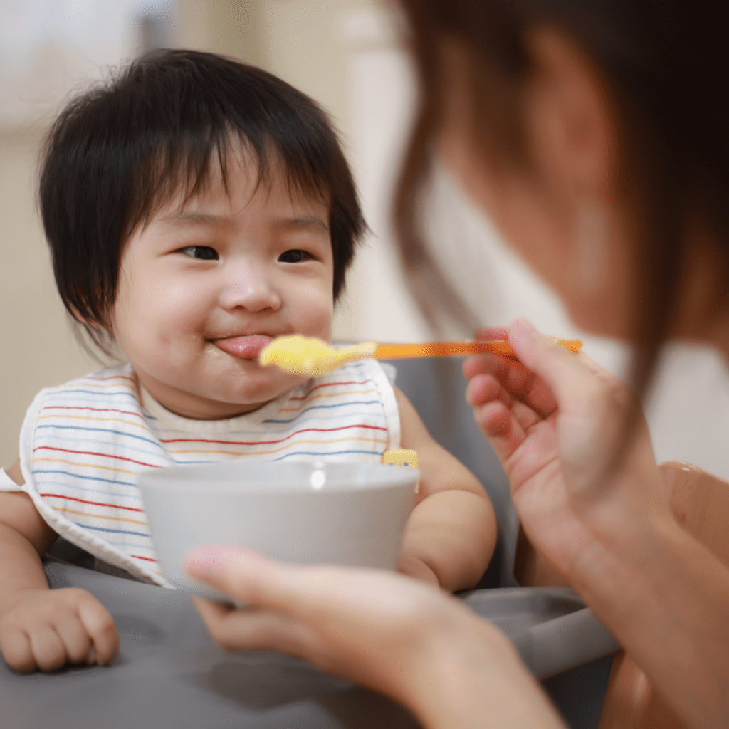 Baby being offered pureed food, has tongue forward out of mouth to push food out.