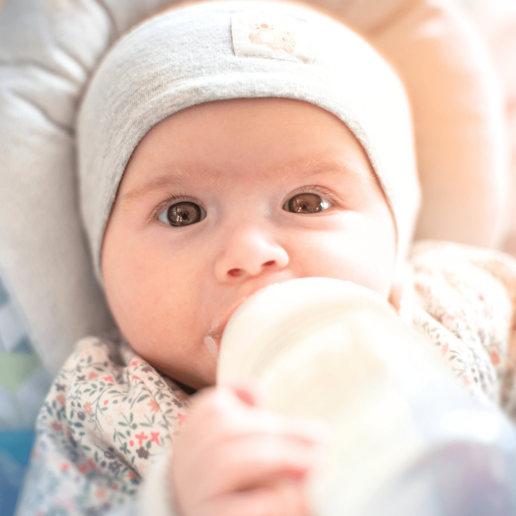 A close up photo of a baby's face while they drink formula from a bottle.