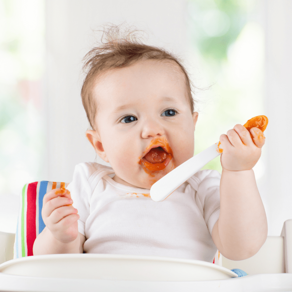Baby self-feeding on purees with a long spoon.