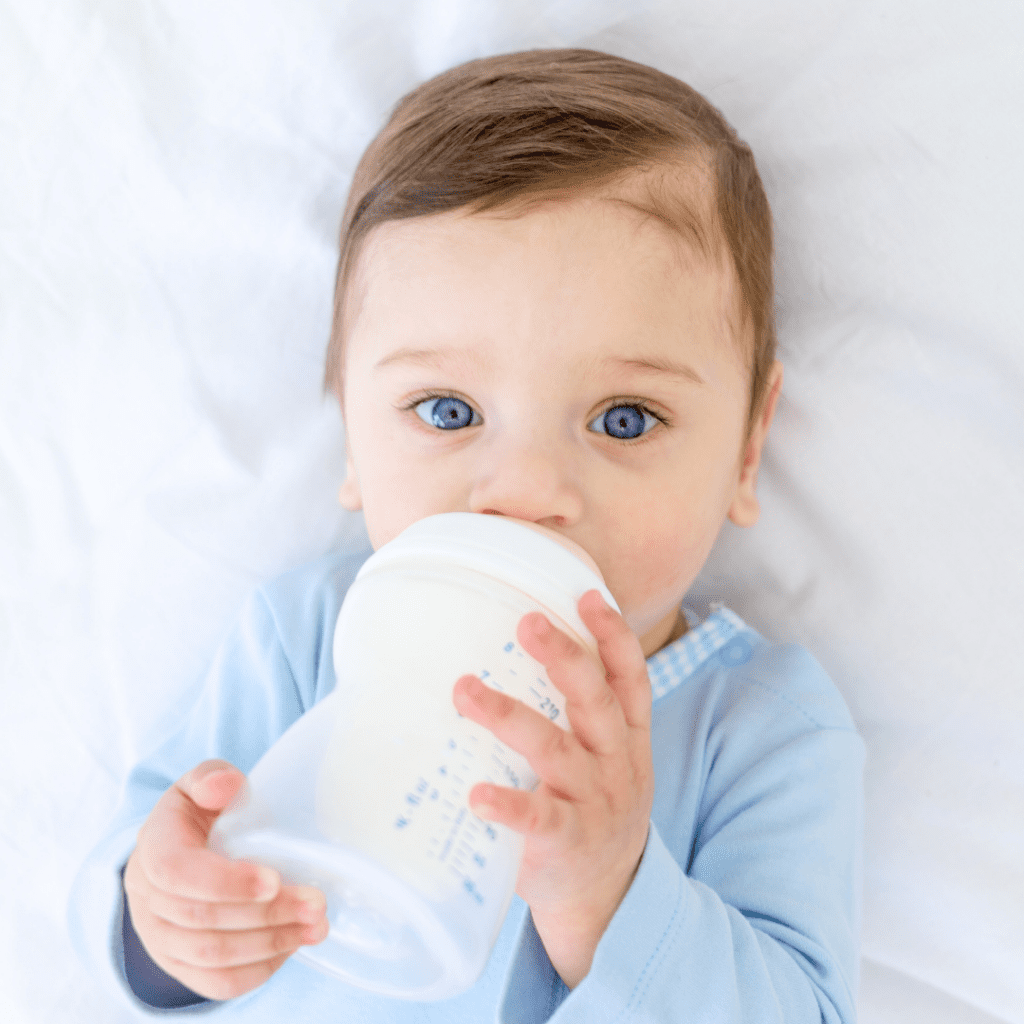 A baby laying down, drinking formula from a bottle.