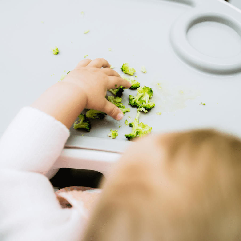 Young babies gag easily, practice is important, this baby practices eating a new texture with cooked broccoli.