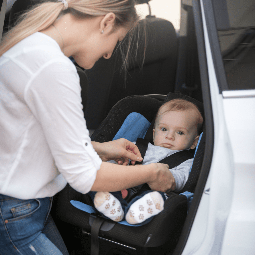 A mother buckles her baby into their car seat.
