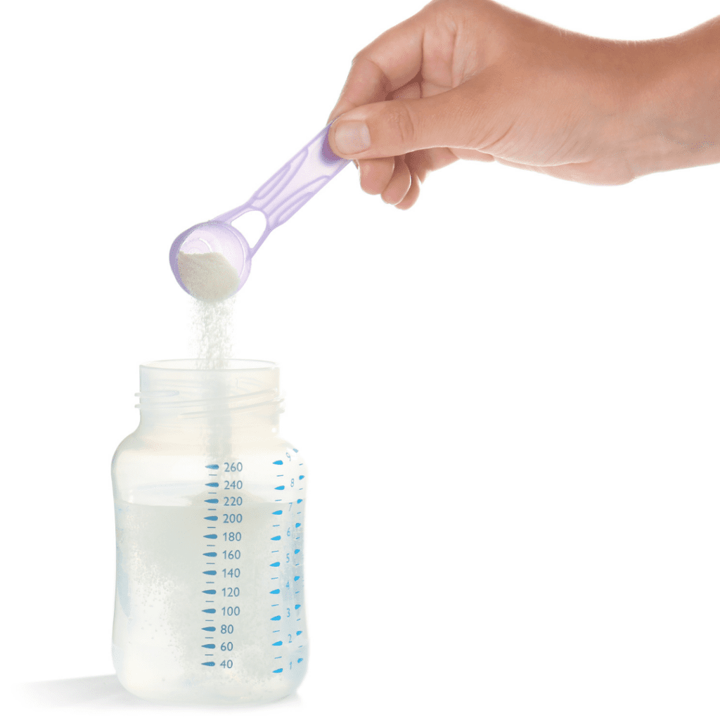 Preparing powdered formula by pouring a scoop into pre-measured water in a baby bottle.