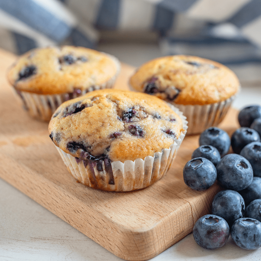 Blueberry muffins on a cutting board with fresh blueberries beside them.
