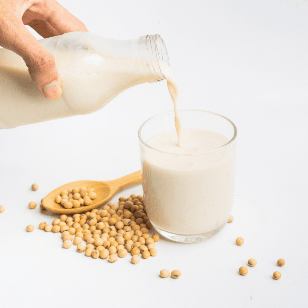A hand pours soy milk from a glass jug into a cup.