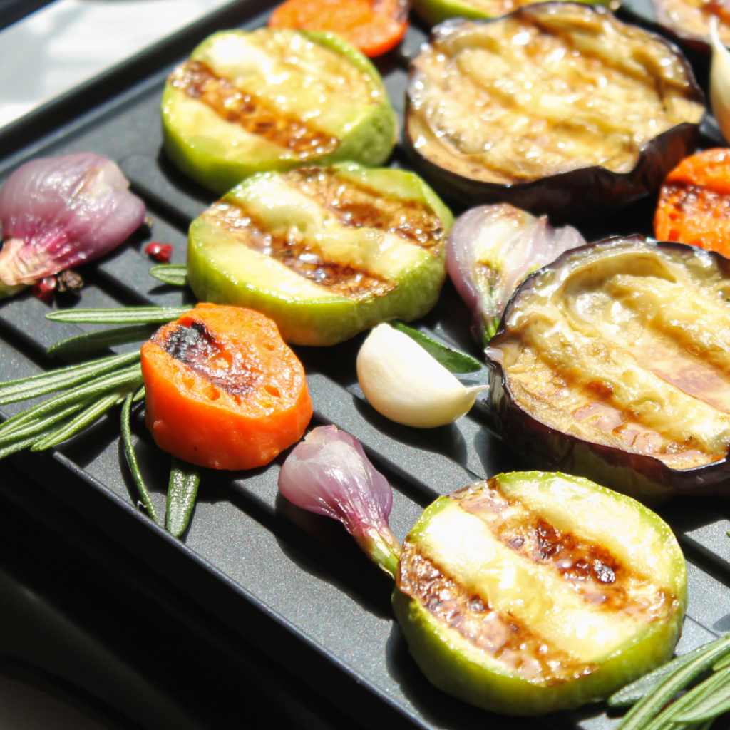 Vegetables on the grill including tomatoes, onion, eggplant, and zucchini.