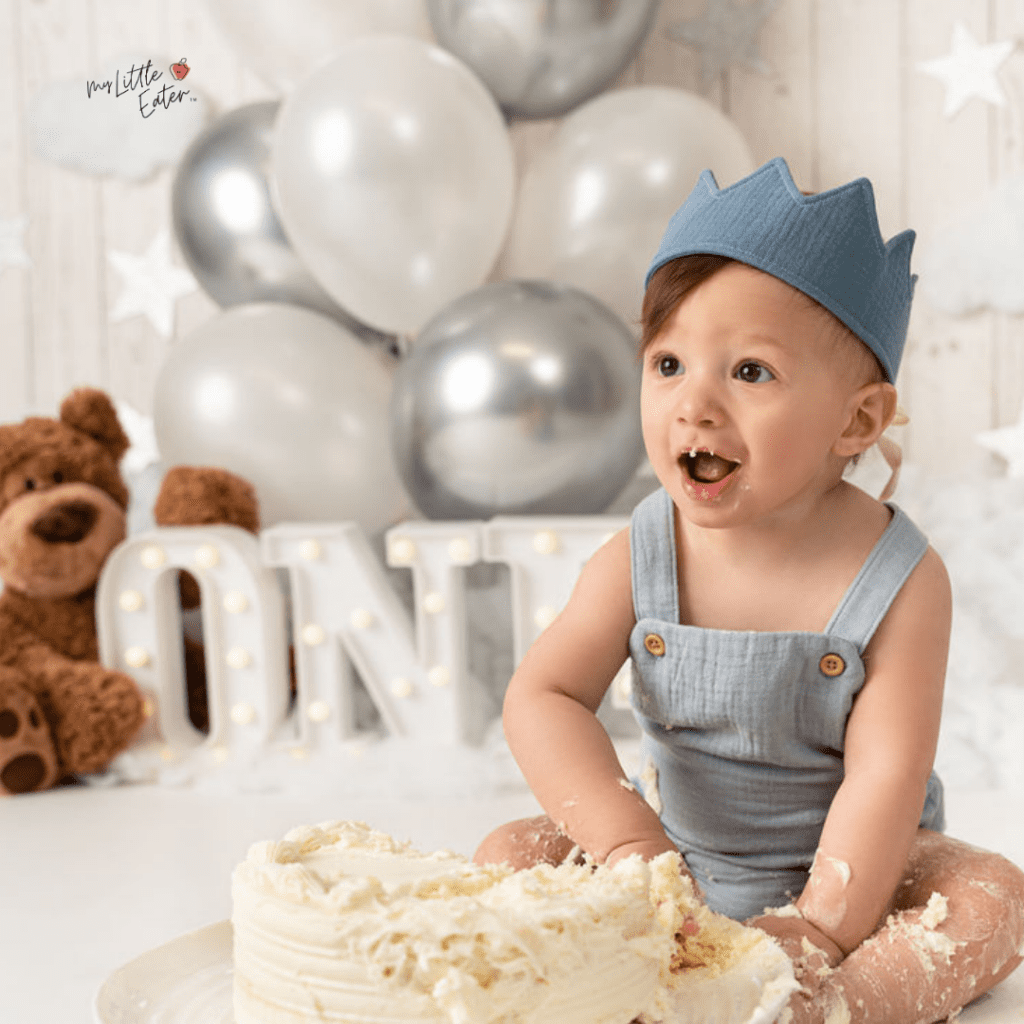 Baby enjoying their first birthday smash cake while wearing a birthday crown.