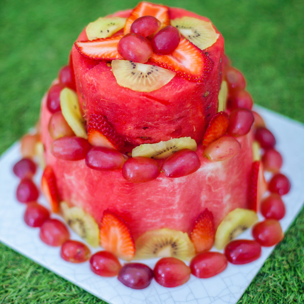 First birthday cake made entirely of fruit cut in different shapes, including: watermelon, grapes, kiwi, and strawberries.