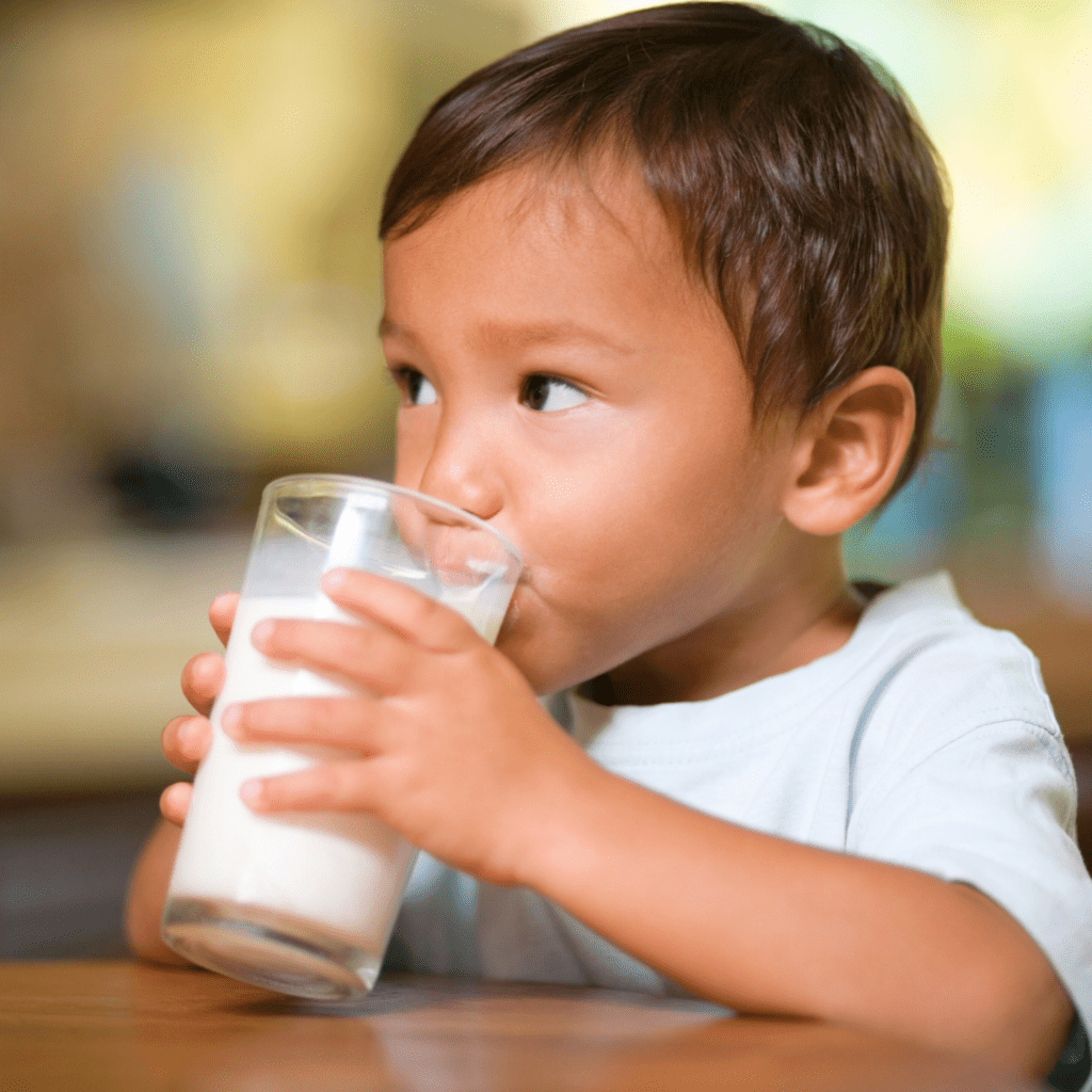 Toddler sitting at the table drinking a glass of cow's milk.