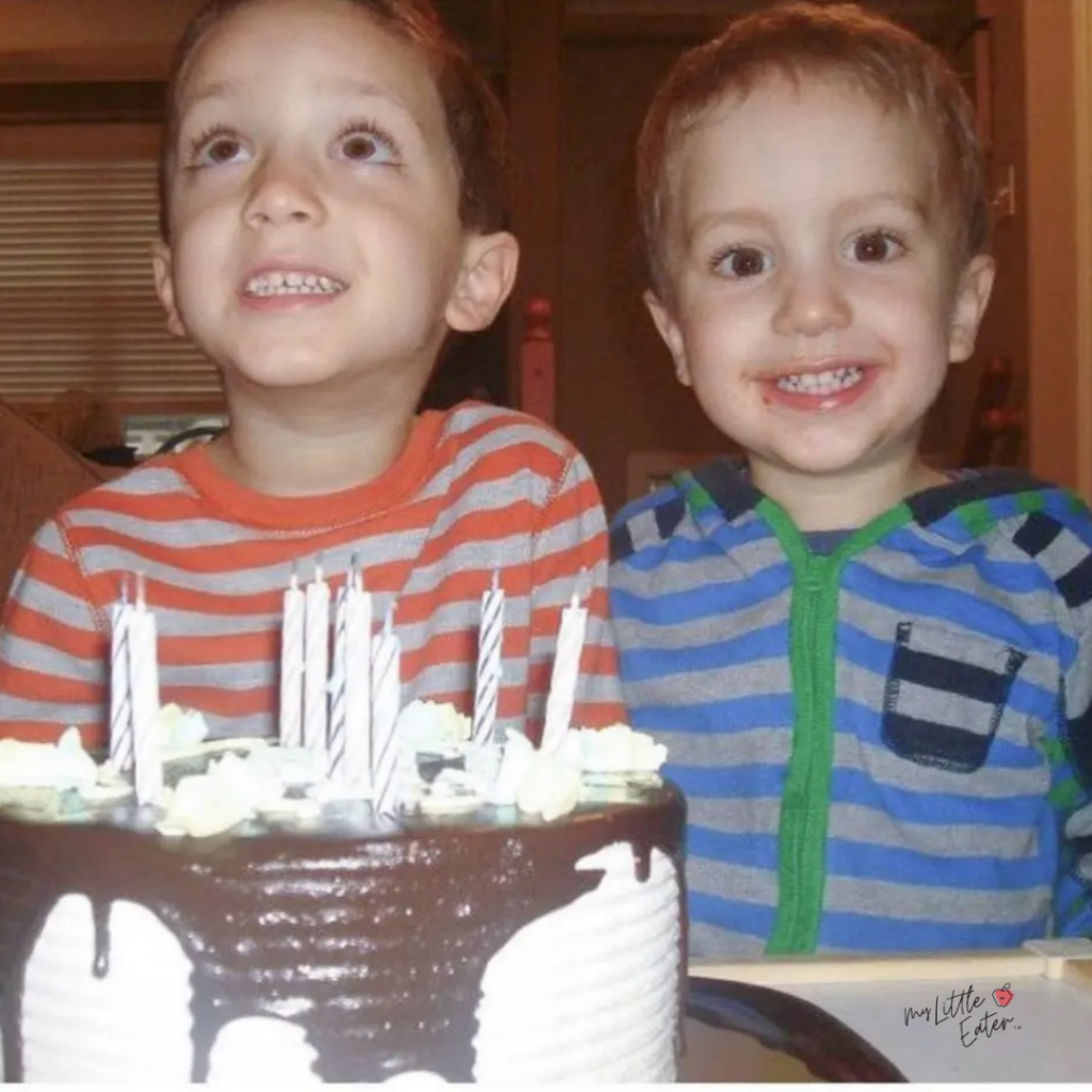 Two kids smile with a smash cake for baby's birthday in front of them.