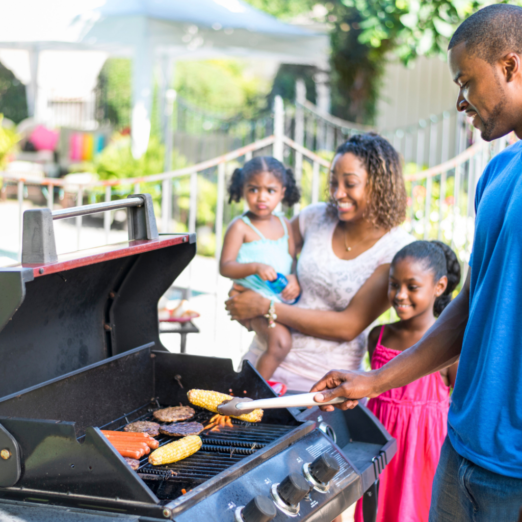 A family cooking burgers, hot dogs, and corn on the barbecue.