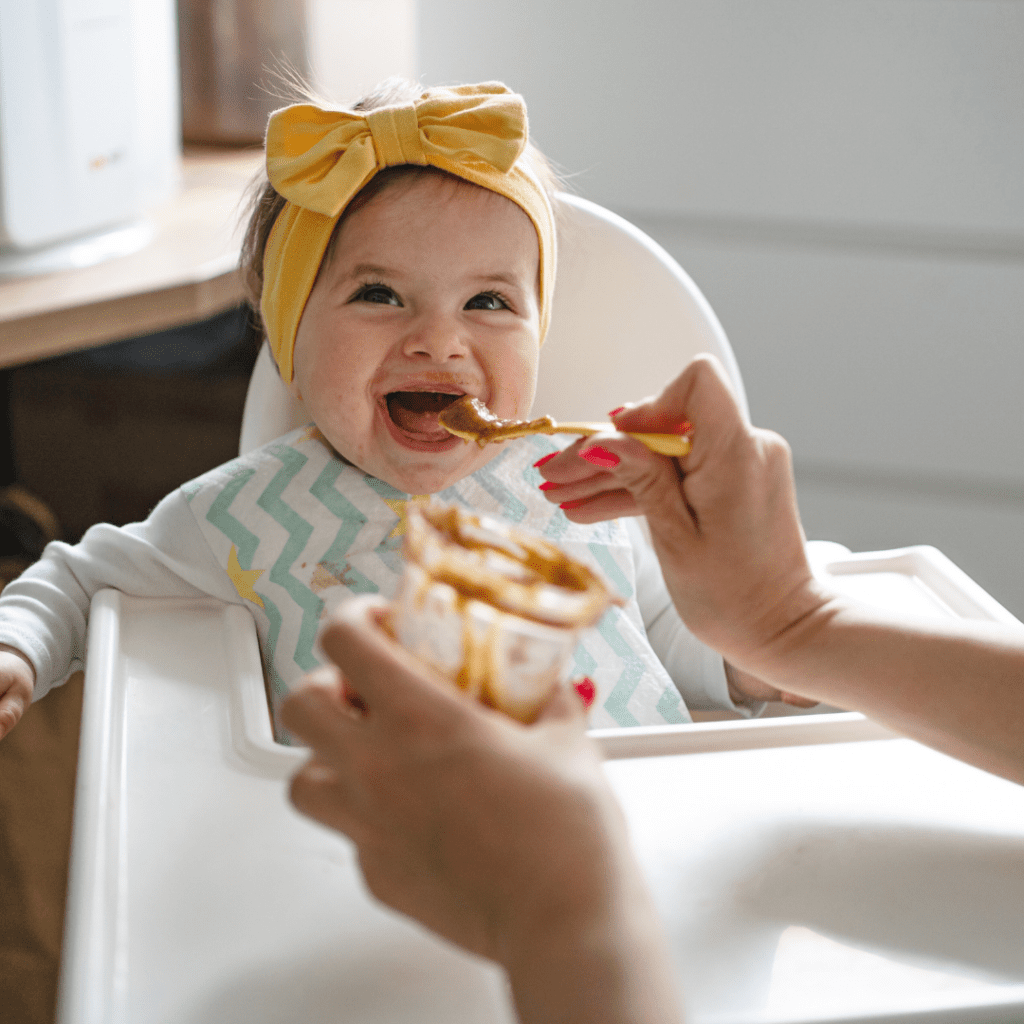 A baby being fed purees mixed with warm breast milk while sitting in a high chair.