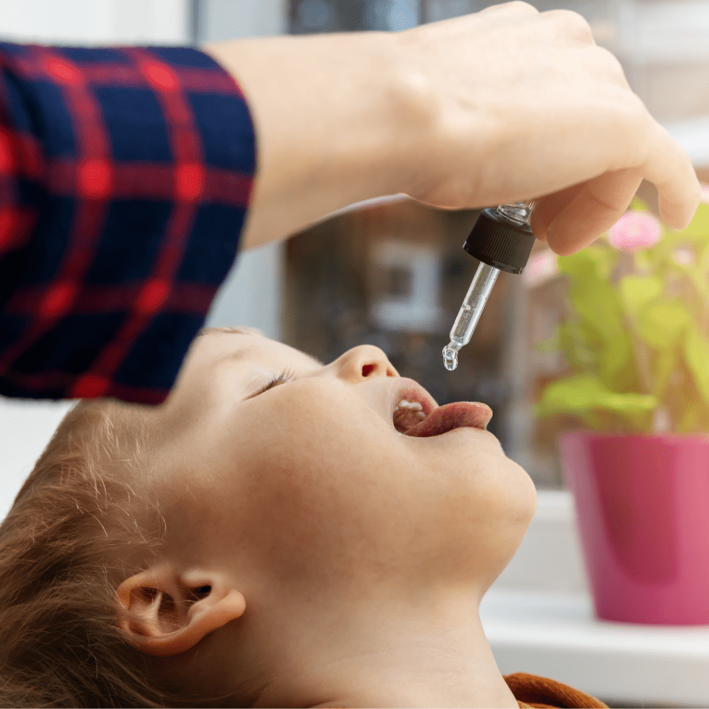 Toddler sticking tongue out as a drop of liquid falls from a medicine dropper.