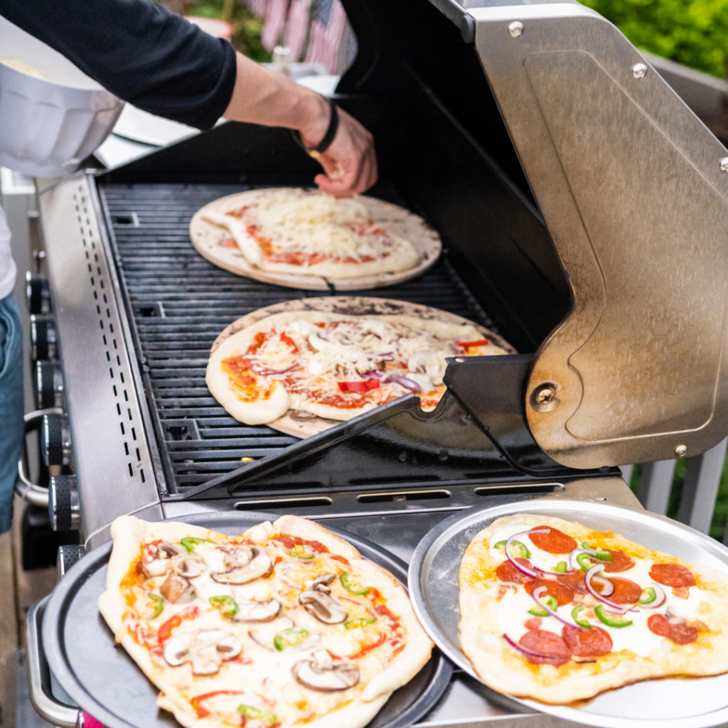 Four different pizzas being cooked on a barbecue.