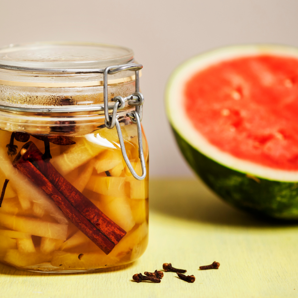 Pickled watermelon rinds in a sealed jar with half a watermelon behind it.