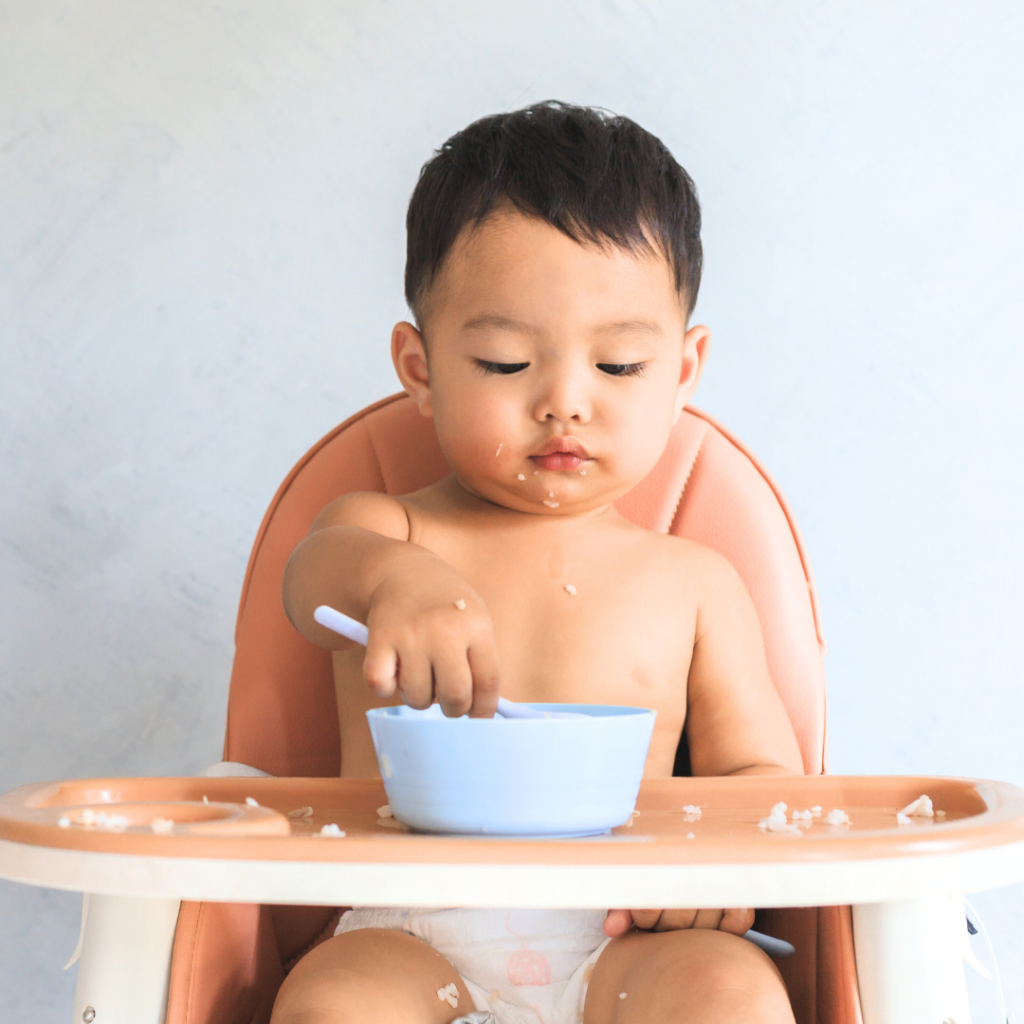 Baby eating from a spoon independently while sitting in a high chair.