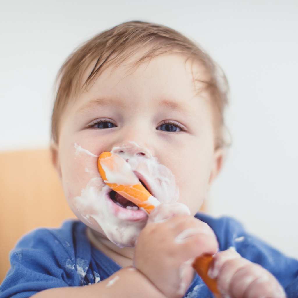 Baby with too much food on their face as they learn to bring food to their own mouth with a spoon.