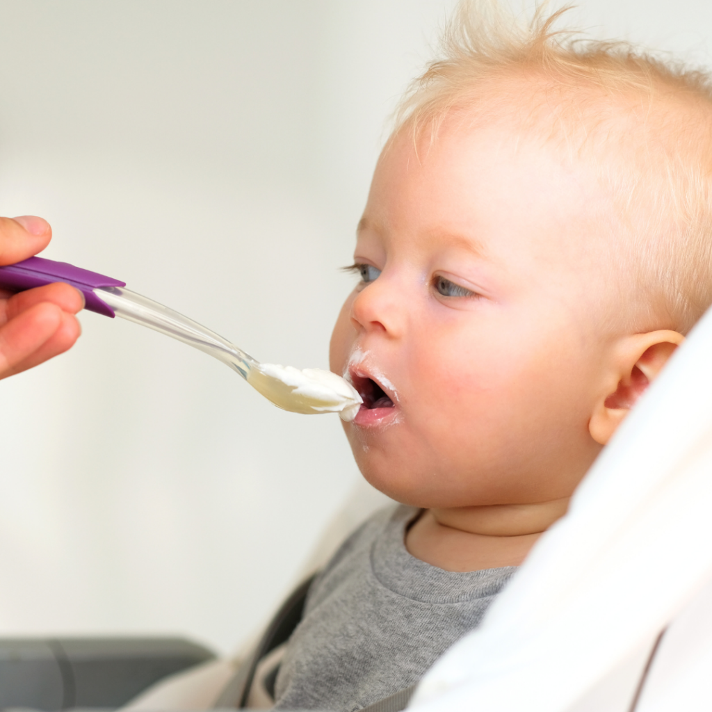 Baby approximately 6 months of age being spoon-fed Greek yogurt.