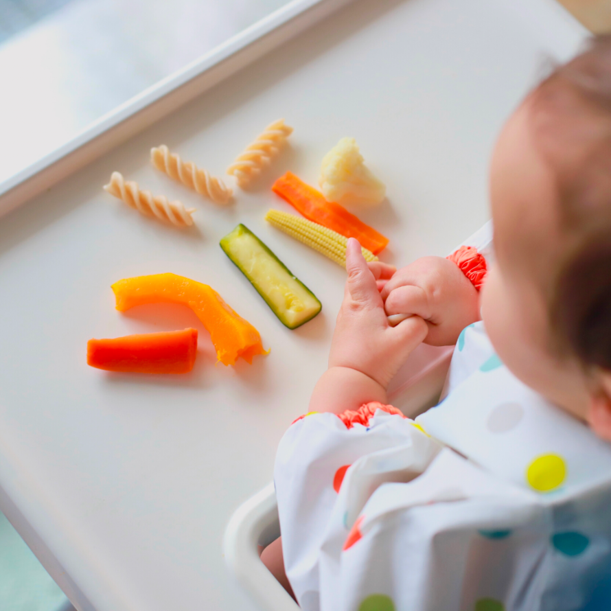 Baby eating various finger shaped foods such as pepper and rotini pasta for baby led weaning.