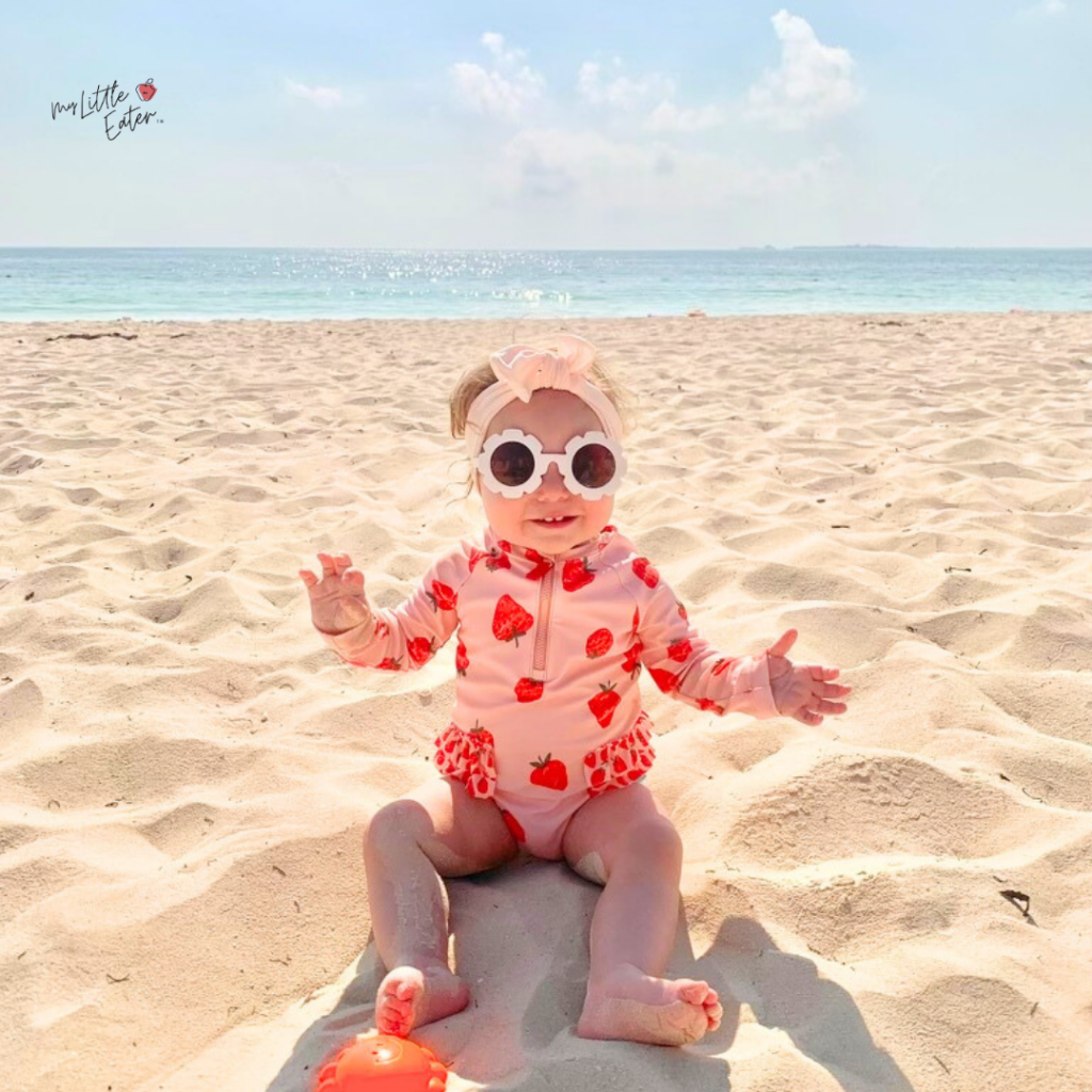 Aila sitting in the sand at the beach in Mexico on a hot day.