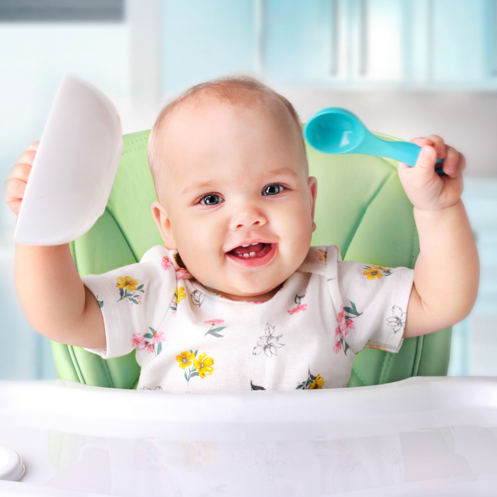 Baby sitting in high chair while holding a bowl and a spoon up in the air excitedly.