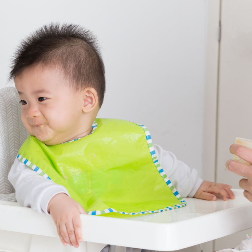 Baby sitting in a high chair turning their head away from puree as a sign of fullness.