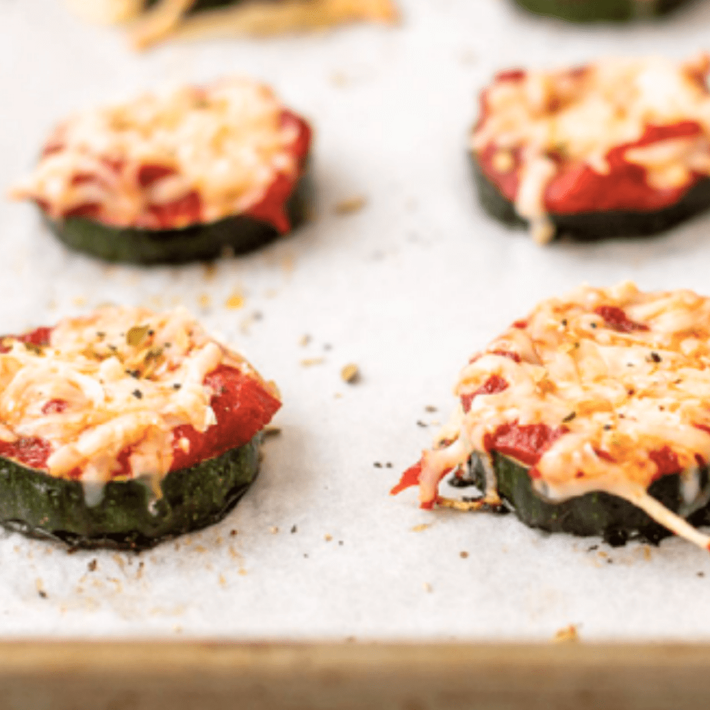 Melted cheese on top of slices of zucchini with tomato sauce for a toddler snack or meal.