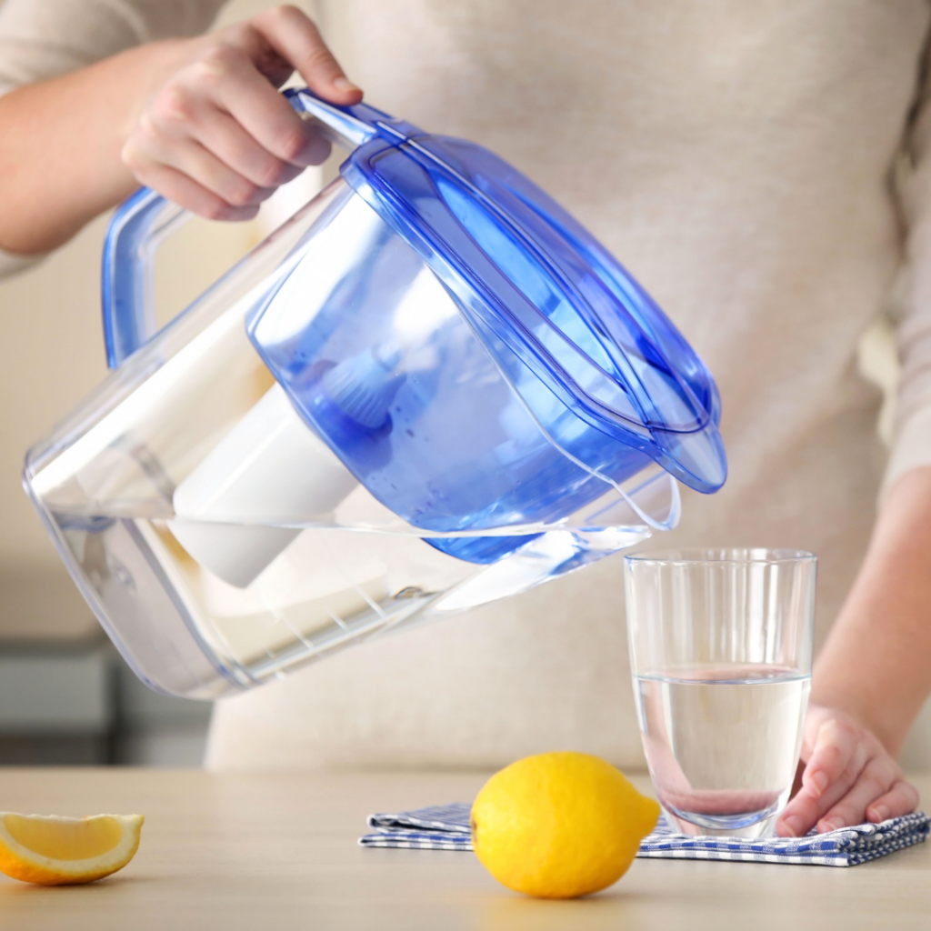 Woman pouring water from a blue filtered water jug into a clear glass. 