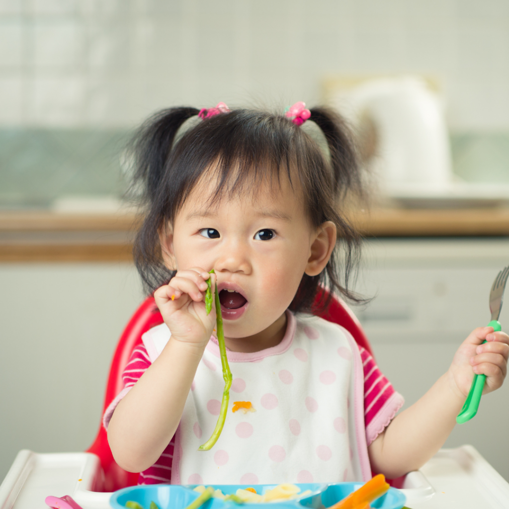 Baby eating asparagus spears in their high chair.