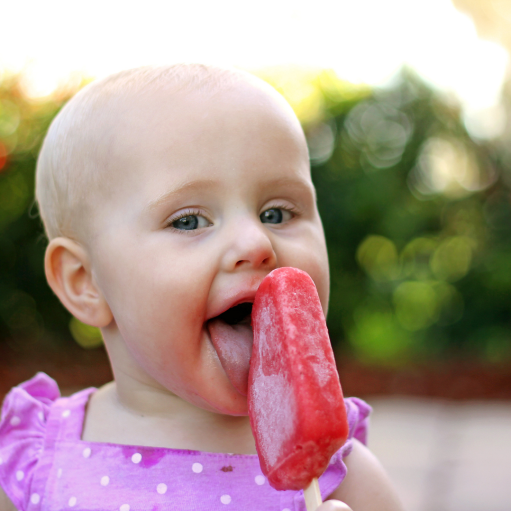 Baby licking a red popsicle.