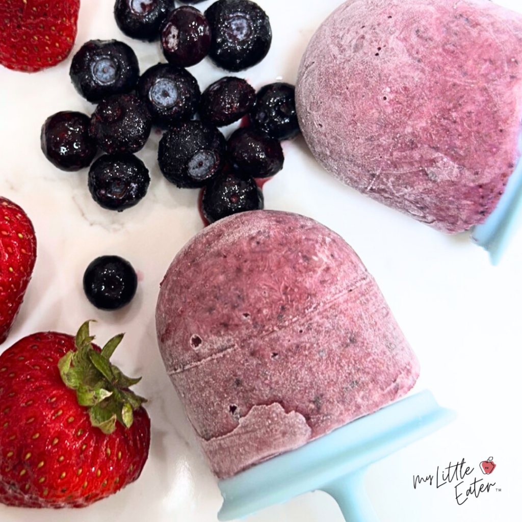 Two purple popsicles with strawberries and blueberries.