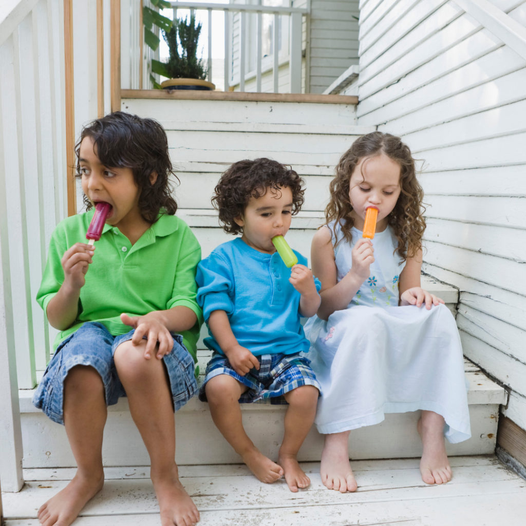 Siblings sitting on steps eating popsicles.