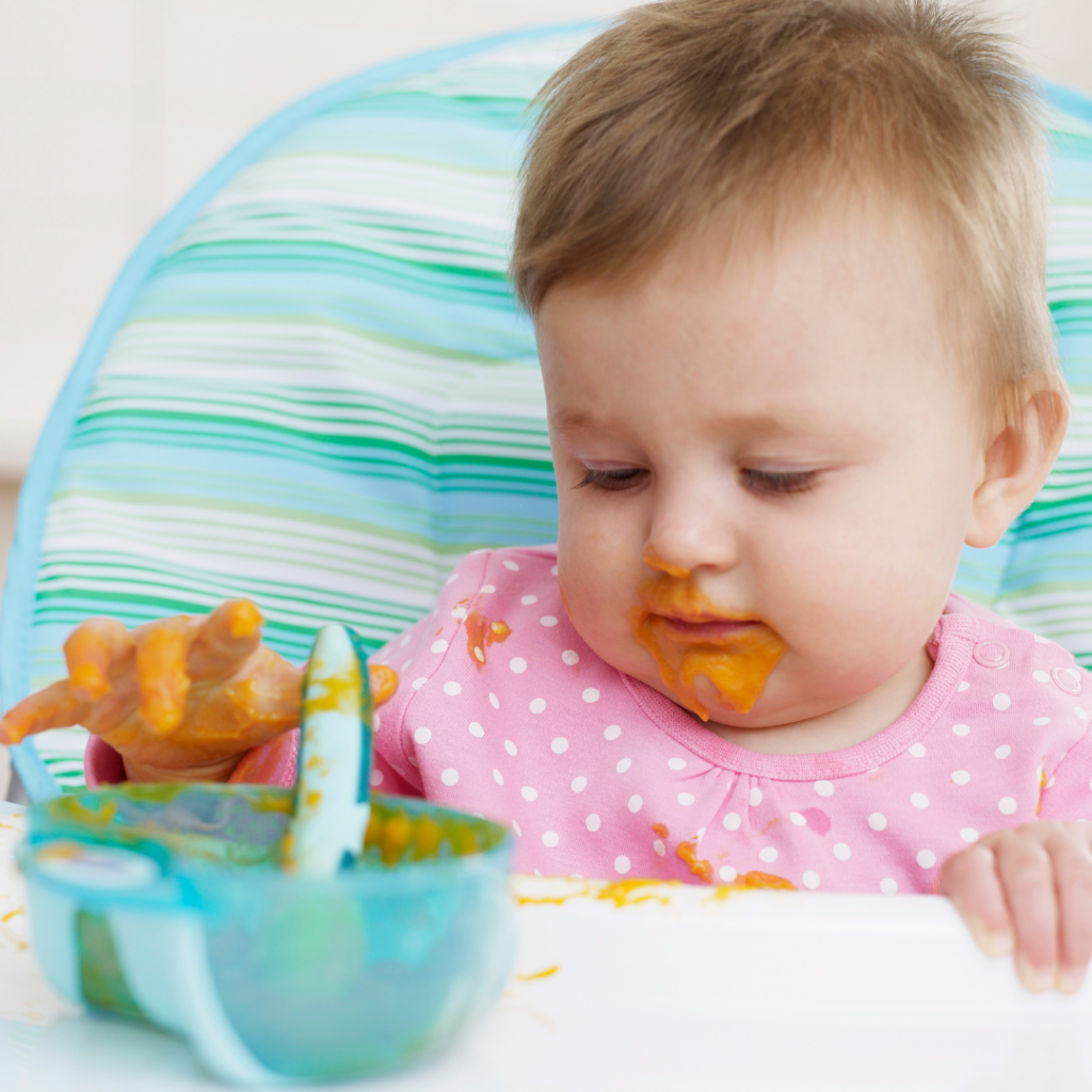 A messy baby playing in their bowl of baby food after eating solids.