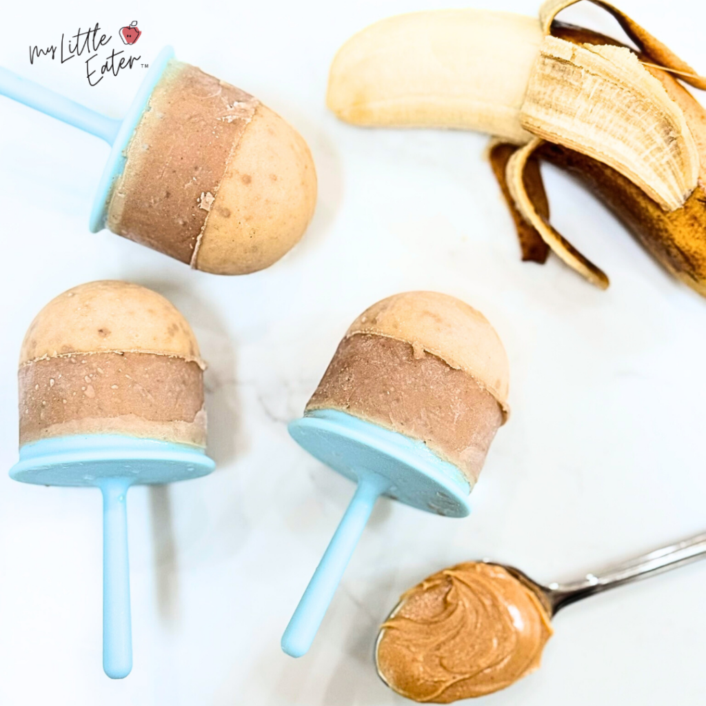 Banana and peanut butter on a spoon with 3 brown popsicles.