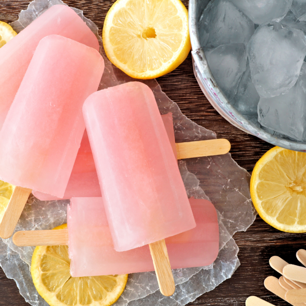 Pink lemonade popsicles with lemon slices in the background.