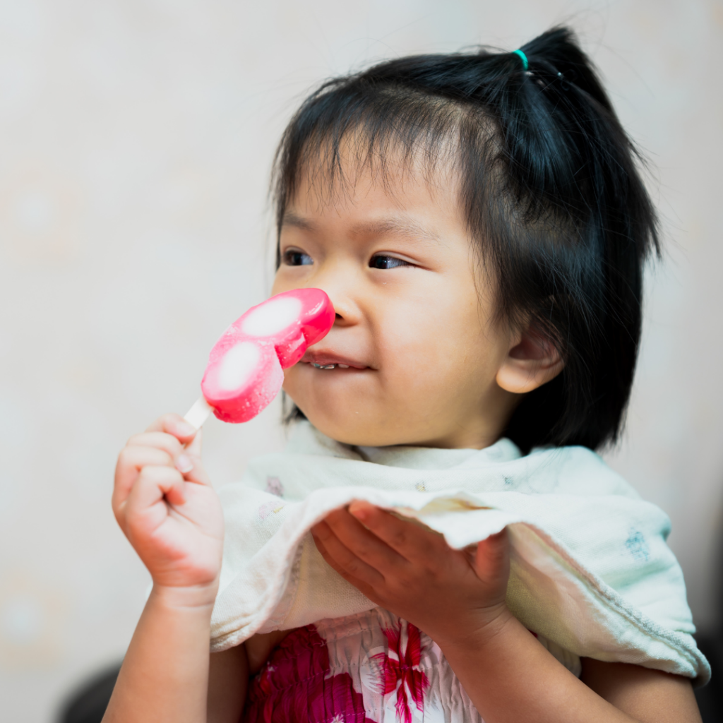 Baby eating a pink and white popsicle.