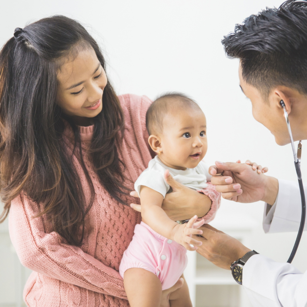 A baby being held by their mom while being examined by their doctor.