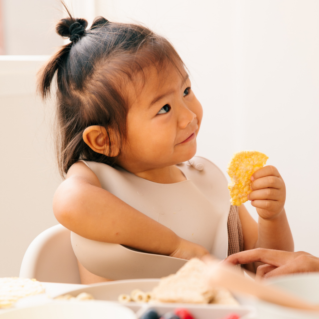 Baby smiling while eating breakfast using the baby led weaning style, in her highchair.