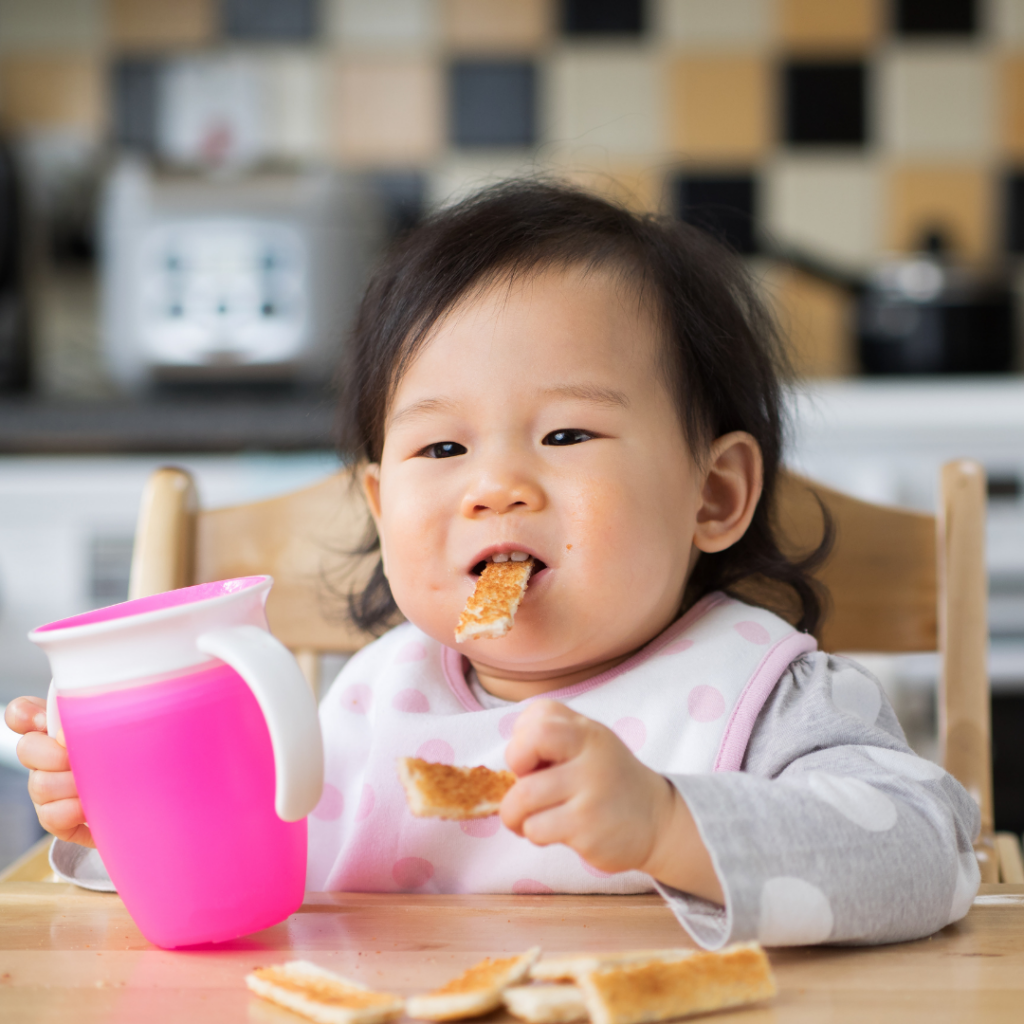 Baby sitting in high chair eating toast strips.