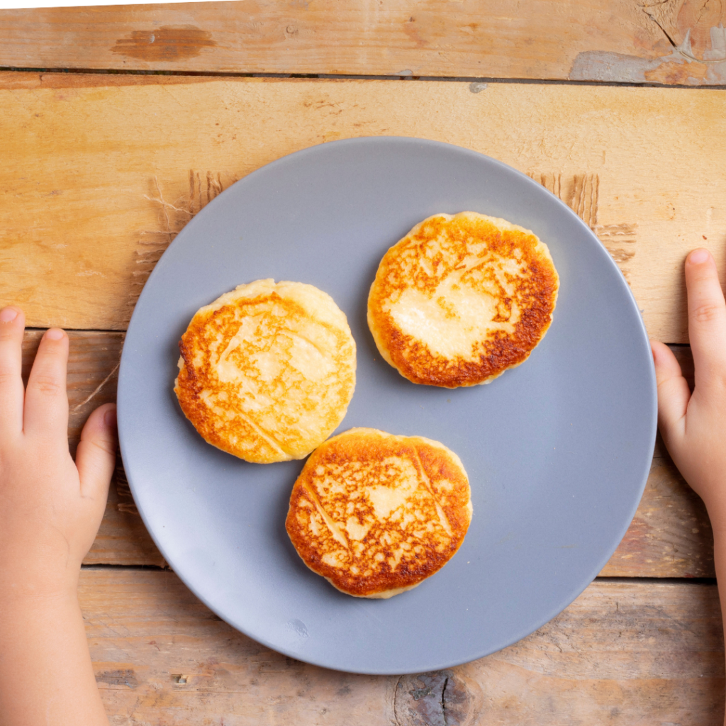 Baby's hands on either side of a plate of pancakes.