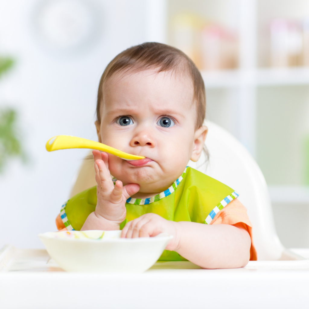 Baby with a quizzical look while holding a spoon in their mouth.