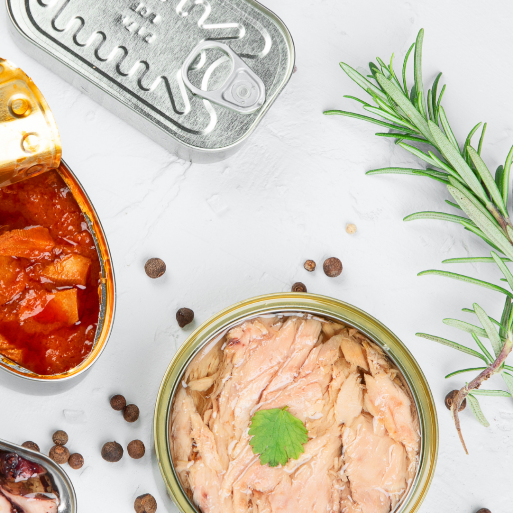 Top view of canned salmon and other canned foods on a light background.