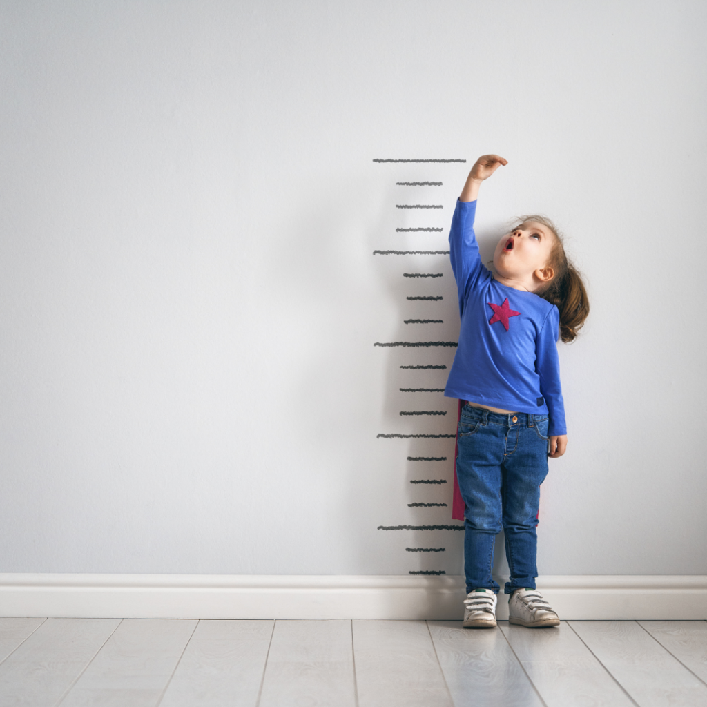 A child holds their hand over their head in a measurement of height.