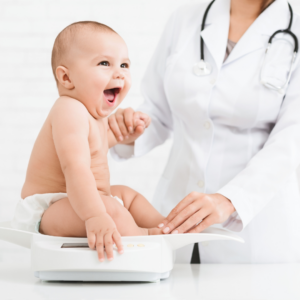 Baby smiles while being weighed by a doctor, note that breastfed babies gain weight faster in the first 6 months and this baby is approaching that age.