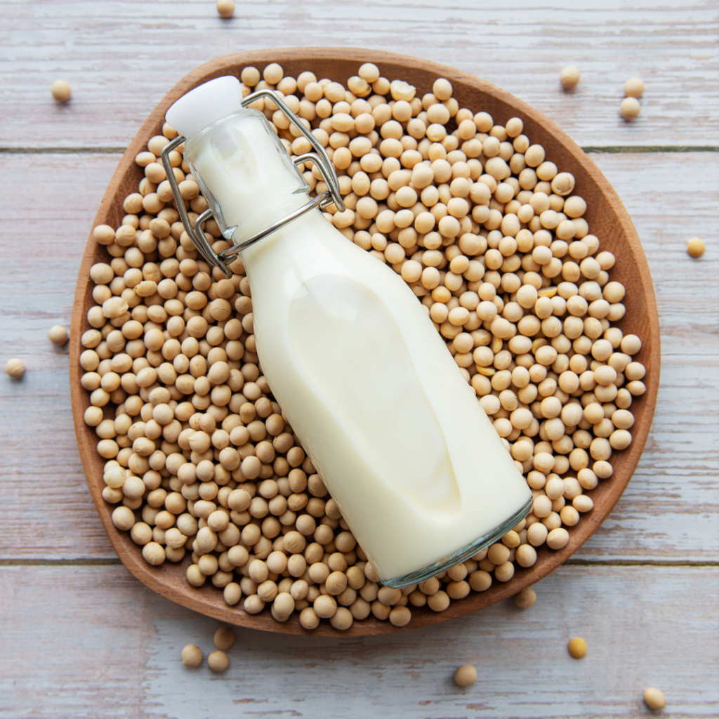 Soy beans in a bowl with a bottle of soy milk laying on top.