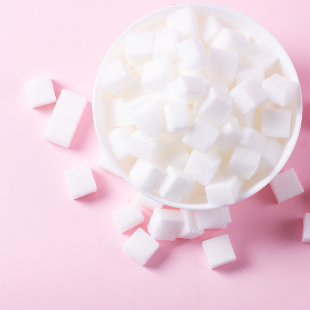 Sugar cubes in a white bowl on a pink background.